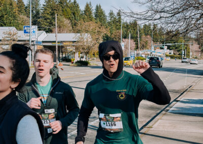 Runners wearing race bibs and green outfits moving down the street during the 2025 Poulsbo Beer Run.