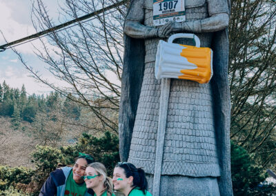 Participants posing at the Norseman statue decorated with a race bib and inflatable beer mug during the 2025 Poulsbo Beer Run.