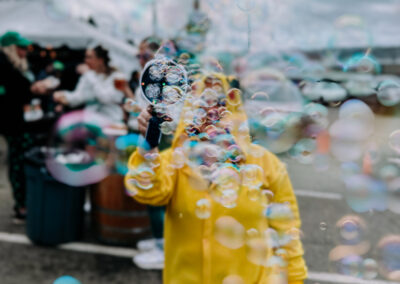 Person wearing a yellow rain suit blowing bubbles into the air at the 2025 Poulsbo Beer Run.